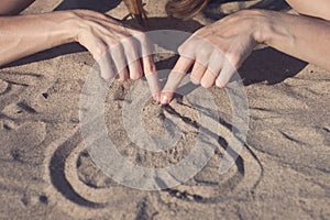 Female hands draw heart on dry sand on the beach on a sunny day