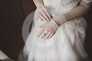 The female hands of the fair-skinned bride lie on the white wedding dress