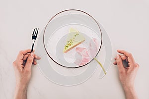 Female hands, flower and piece of cake on plate on white tabletop