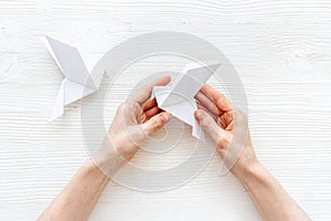 Female hands folding sheet of paper - origami bird. Overhead view