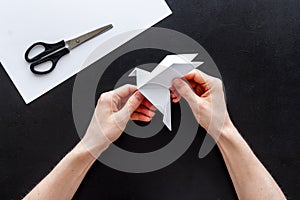 Female hands folding sheet of paper - origami bird. Overhead view