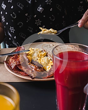 Close-up of hands eating scrambled eggs, bacon, toast and juice