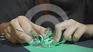 Female hands gently frizzing thinly fringed green paper with metal scissors.