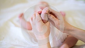 Female hands gently massage the foot of the baby. Mom light stroking  leg of small child. Close up.