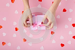 Female hands with a gift box on a pastel colored background top view, the girl opening a present and untying a ribbon bow, the