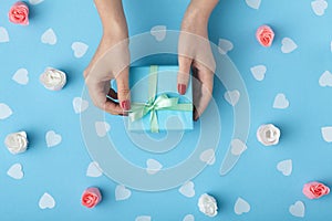 Female hands with a gift box on a pastel colored background top view, the girl opening a present and untying a ribbon bow, the