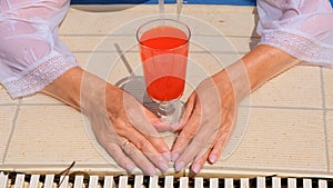 female hands with a glass of pink cocktail by the swimming pool, close-up. Summer mood concept, hotel relaxation, all