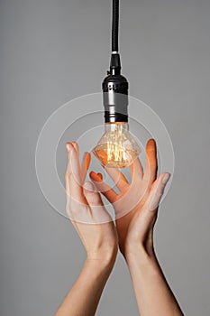 Female hands with glowing light bulb on grey background