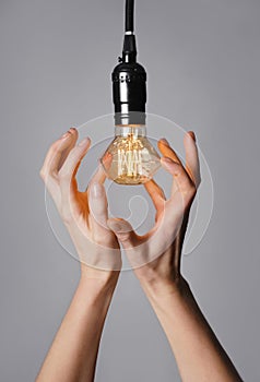 Female hands with glowing light bulb on grey background