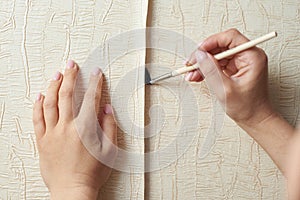 Female hands glues torn-off wallpaper on the wall