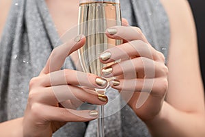 Female hands with gold nail design. Gold glitter nail polish manicure. Woman hold champagne glass