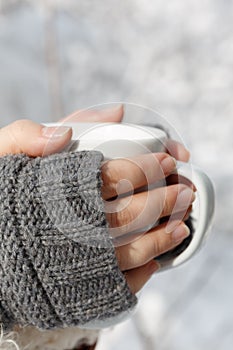 Female hands in gray fingerless mittens with white cup of tea in