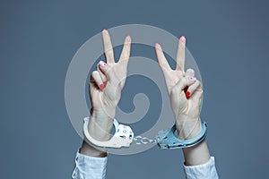 Female hands with handcuffs showing victory sign on gray background