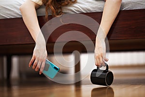 Female hands hanging from a beg in a bedroom, holding phone and empty black cup.