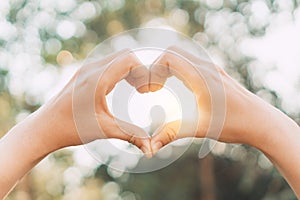 Female hands heart shape on nature bokeh sun light flare and blur leaf abstract background