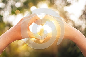 Female hands heart shape on nature bokeh sun light flare and blur leaf abstract background