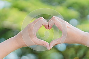 Female hands heart shape on nature bokeh sun light flare and blur leaf abstract background. Copy space of happy love and freedom
