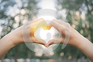 Female hands heart shape on nature green bokeh sun light flare and blur leaf abstract background