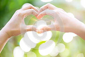 Female hands heart shape on nature green bokeh sun light flare and blur leaf abstract background. Happy love and freedom concept