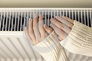 Female hands on a heating radiator, close-up.