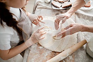 Female hands helping children to make patterns on the dough in the kitchen. Baking cookies