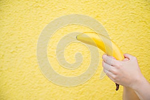 Female hands hold a banana on a yellow background