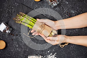 Female hands hold banches of fresh green asparagus on stone background