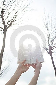 Female hands hold the book against the background of nature. Vertical shot.