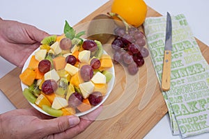 Female hands hold a bowl full of fresh and colorful fruit. Apple, kiwi, orange, papaya, mango, melon. Breakfast or break, healthy