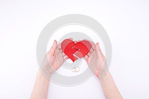 Female hands hold a broken heart on a white background with wedding rings. Relationship problems in marriage, divorce