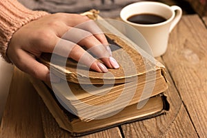 Female hands hold a coffee cup and an old open book.