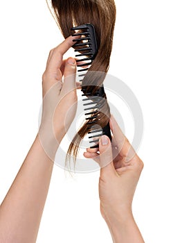 Female hands hold a comb around which long natural brown hair is wound, combing