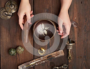 Female hands hold a copper Tibetan singing bowl and a wooden stick