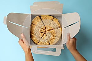 Female hands hold delivery box with Napoleon cake on blue background