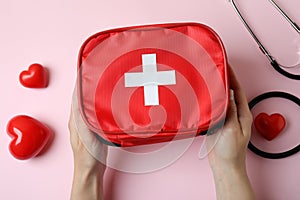 Female hands hold first aid medical kit on pink background