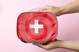 Female hands hold first aid medical kit on pink background