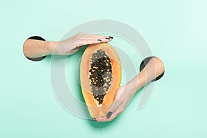 Female hands hold fresh papaya through a hole on neon mint background. Minimalistic creative isolated concept.