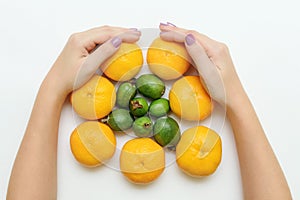 Female hands hold fresh tangerines and feijoaon white background. Froot flat lay top view