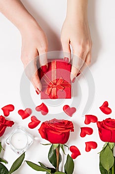 Female hands hold a gift box for valentine& x27;s day. Red roses and candles on a white background.