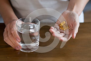 Female hands hold a glass of water and fish oil tablets Omega-3 fatty acid capsules. Taking vitamins and supplements close-up