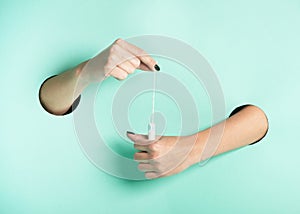 Female hands hold hygienic tampon through a hole on neon mint background. Minimalistic creative isolated concept.