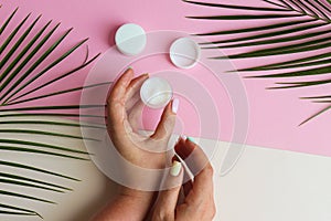 Female hands hold a jar of body cream on a pastel pink and beige background. Beauty and cosmetic concept. Top view, flat