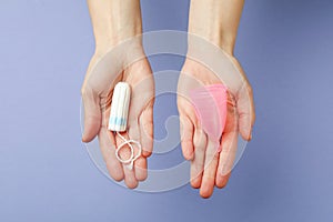 Female hands hold menstrual cup and tampon on violet background