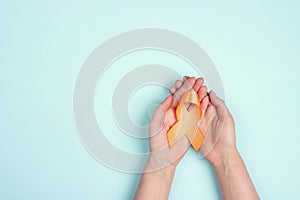 Female hands hold an orange awareness ribbon on a blue background. World Multiple Sclerosis Day