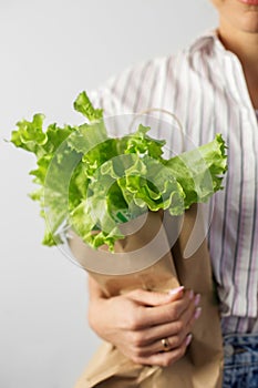 Female hands hold a packet with lettuce on a gray background. Organic food