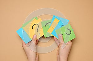 Female hands hold paper sheets with a drawn question mark on a beige background