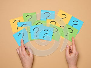 Female hands hold paper sheets with a drawn question mark on a beige background