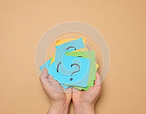 Female hands hold paper sheets with a drawn question mark on a beige background