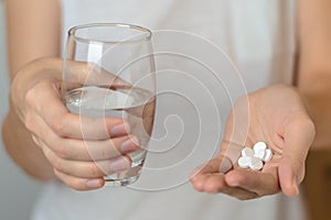 female hands hold pills and a glass of water