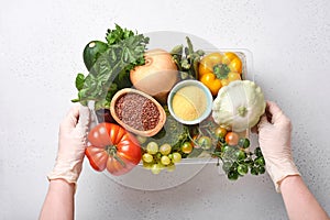 Female hands hold plastic box with assortment of fresh vegetables, fruits, cereals and seeds on old wooden background. Safe home d